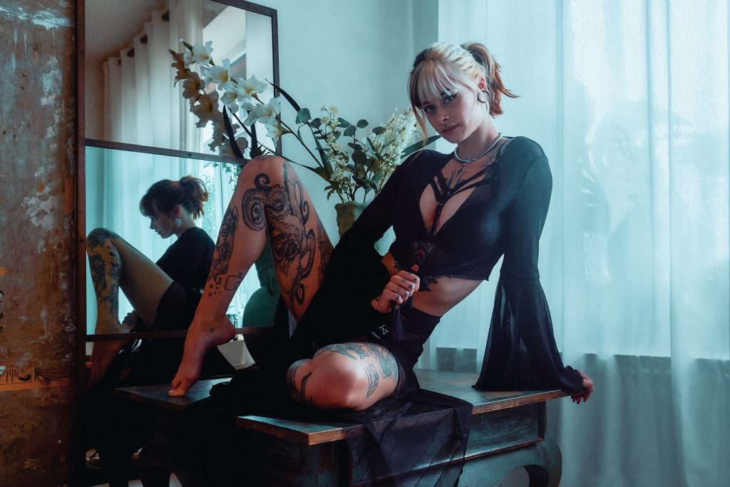 SallyDinosaur lounges in a black outfit in front of a mirror and looks seductively into the camera