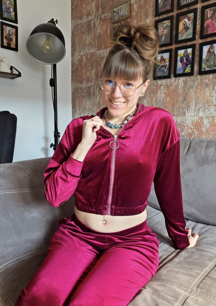 Anne von BettDuett lächelt auf dem Sofa im roten Samtanzug