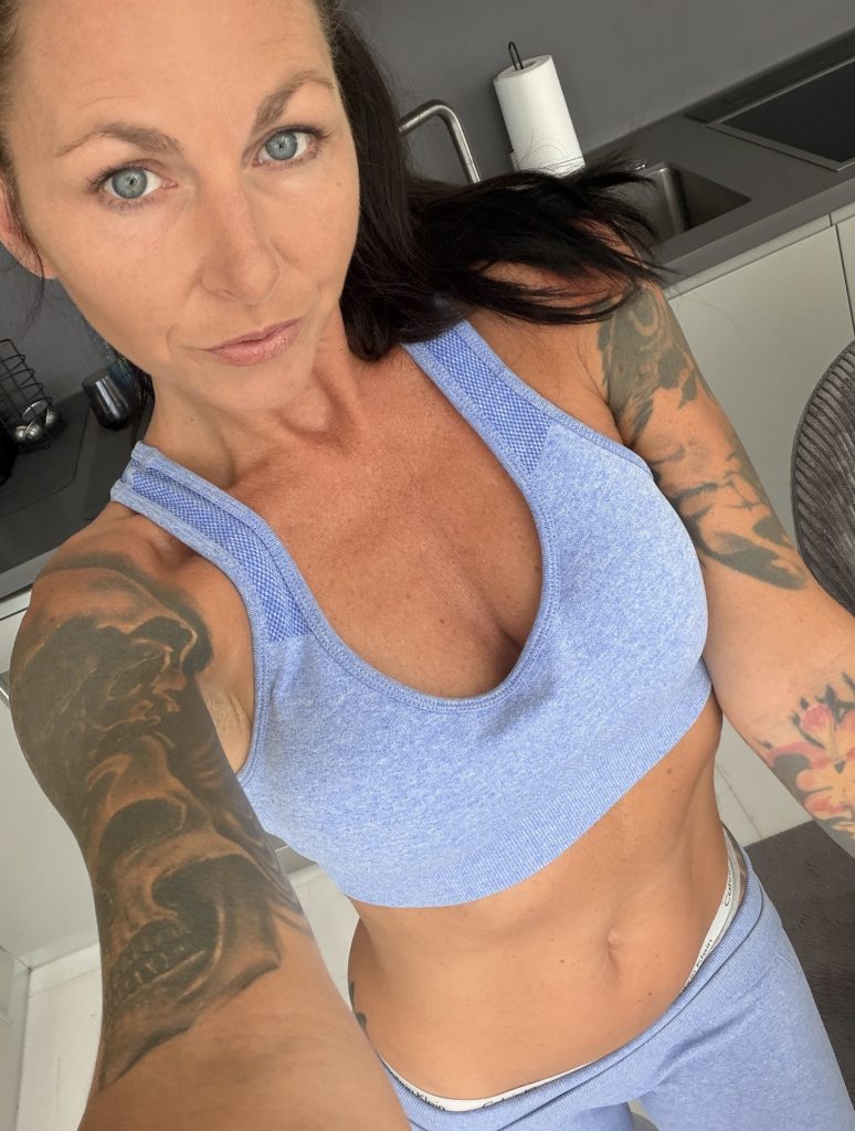 Thirteen-Mel with dark hair and tattoos in a light-blue sporty outfit in a selfie.