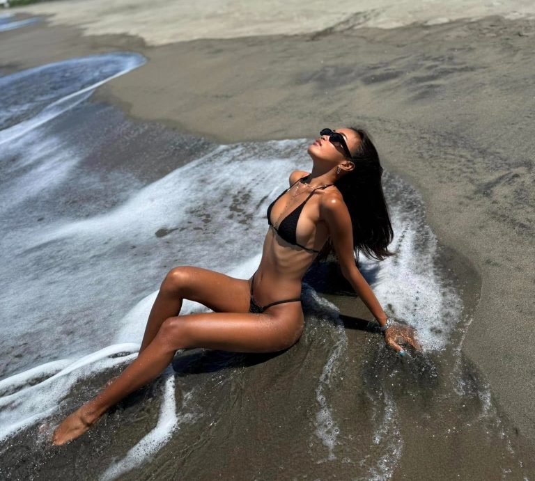 Miyaka Chan sitzt am Strand im Wasser und genießt die Sonne mit tropischem Reisegefühl.