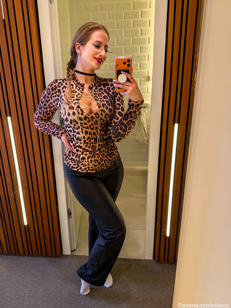 Mika Nox poses in a leopard outfit in front of a mirror and takes a selfie for her FansyMe profile.