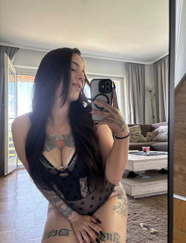 Luna Lynn takes a photo of herself in black transparent lace in front of a mirror in a bright living room.