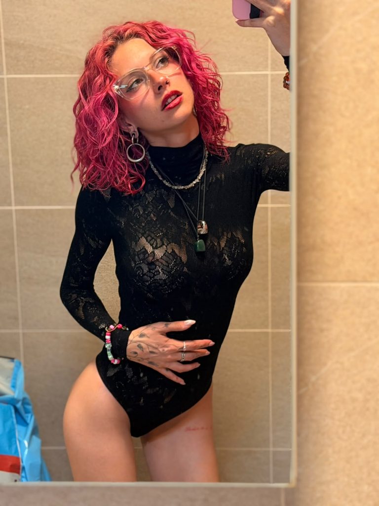 Melanie Jasmin mirror selfie in a black lace bodysuit with pink curls
